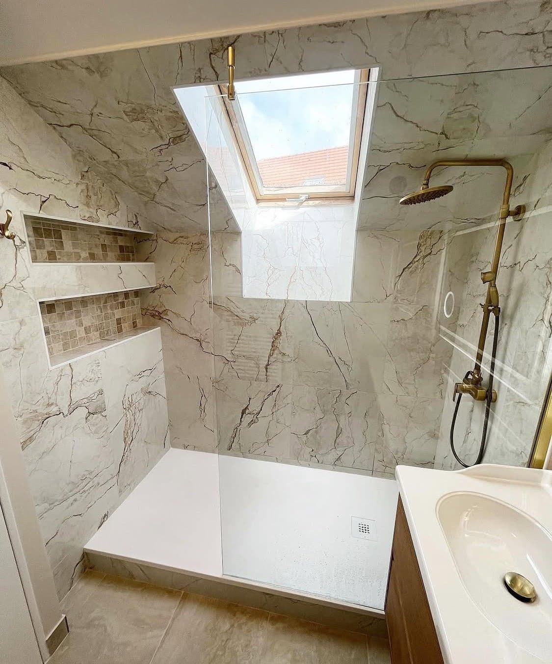 Installation d'une douche spacieuse avec robinetterie dorée en laiton, niches encastrées et carrelage effet marbre lors d'une rénovation salle de bain à Obernai.