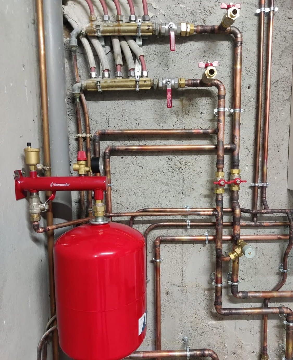 Détail technique des réseaux en cuivre brasés, du collecteur et du vase d'expansion Thermador rouge lors de l'installation d'une nouvelle chaudière à Gaz dans le Bas-Rhin.