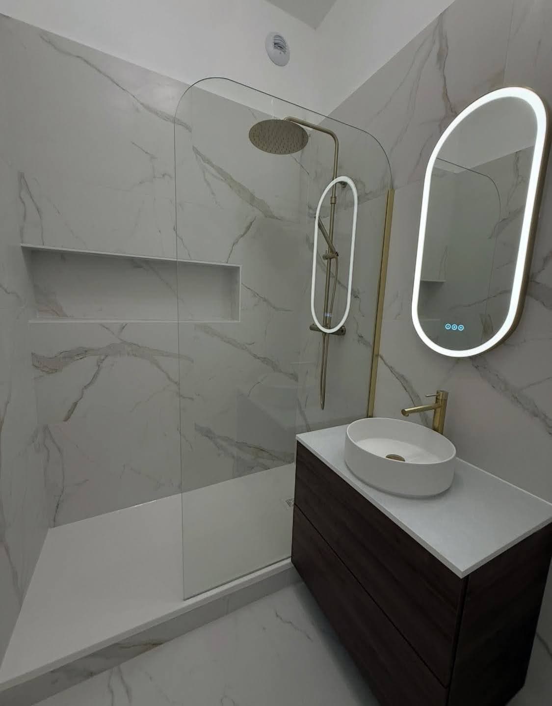 Superbe aboutissement d'une rénovation salle de bain sur mesure à Saverne avec douche italienne, robinetterie dorée, meuble vasque en bois et miroir LED illuminé.
