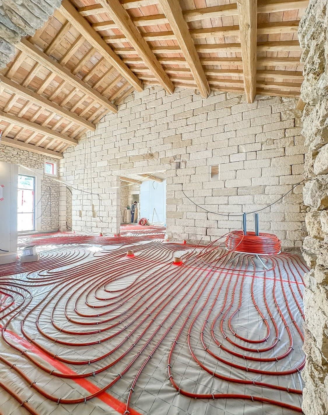 Déroulage minutieux et pose en escargot de tubes PER rouge avec barrière anti-oxygène sur un isolant quadrillé pour une installation d'un chauffage au Sol à Sélestat.
