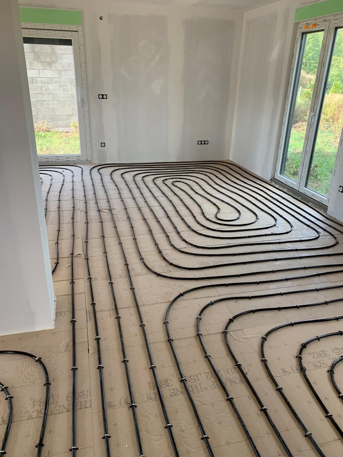 Vue d'ensemble de l'installation d'un plancher chauffant basse température par un chauffagiste Strasbourg dans le salon lumineux d'une maison neuve à Illkirch-Graffenstaden, avec bande résiliente verte apparente.