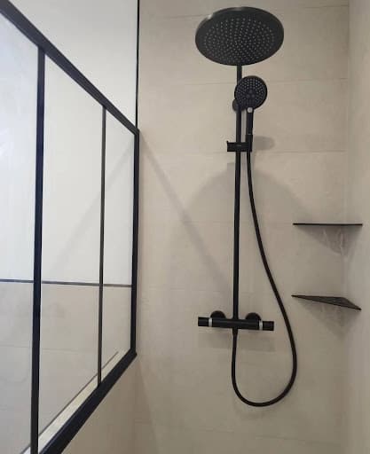 Installation d'une douche moderne avec paroi verrière et colonne de douche noire lors d'une rénovation salle de bain à Strasbourg.