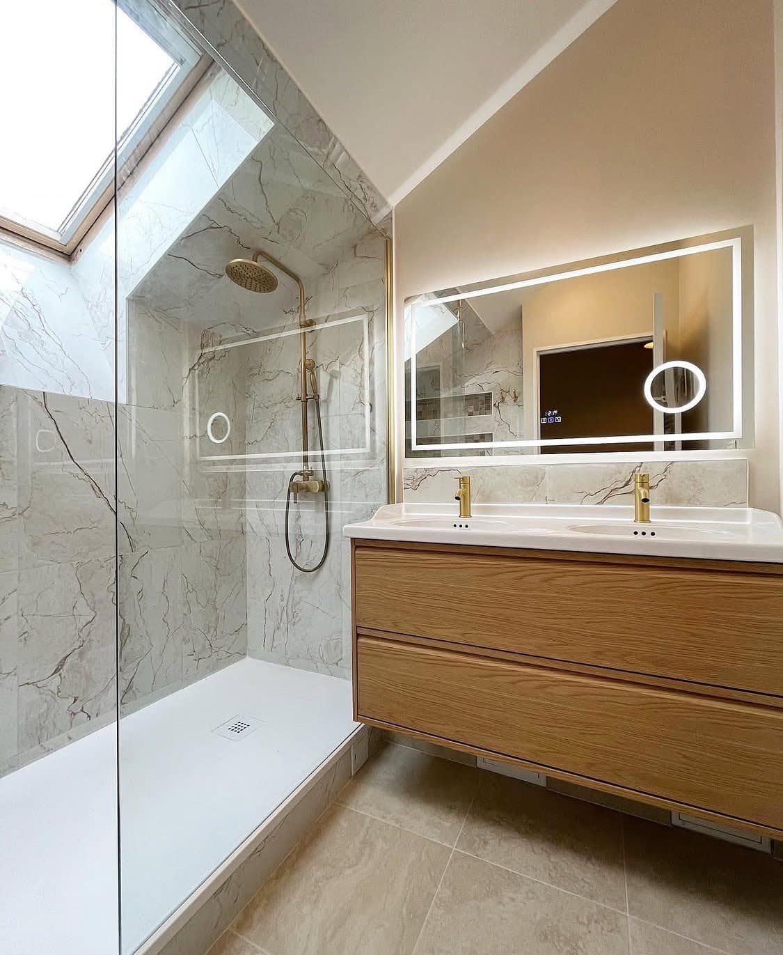 Résultat d'une rénovation salle de bain à Obernai montrant un meuble double vasque suspendu en chêne, un miroir LED et une douche spacieuse aménagée sous les combles.