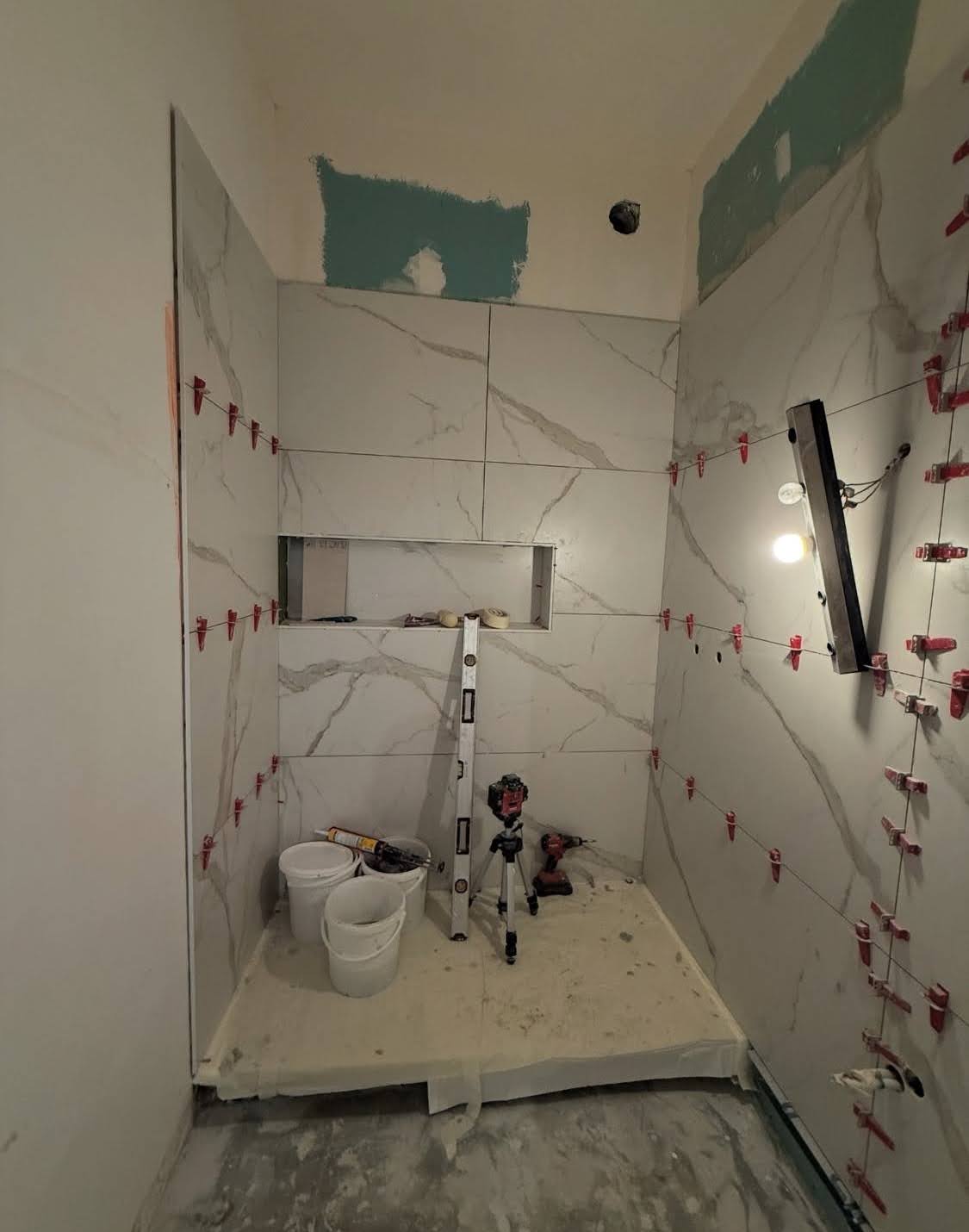 Pose de carrelage grand format imitation marbre avec système de croisillons autonivelants rouges dans le cadre d'une rénovation salle de bain sur mesure à Saverne.