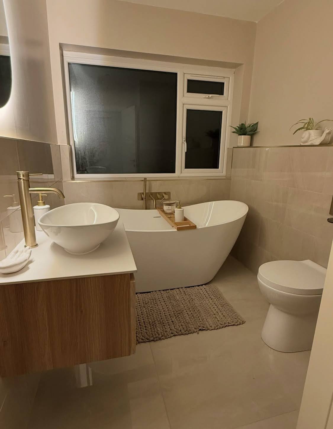 Résultat final d'une rénovation de salle de bain à Schiltigheim avec installation de baignoire îlot, carrelage beige et robinetterie dorée.